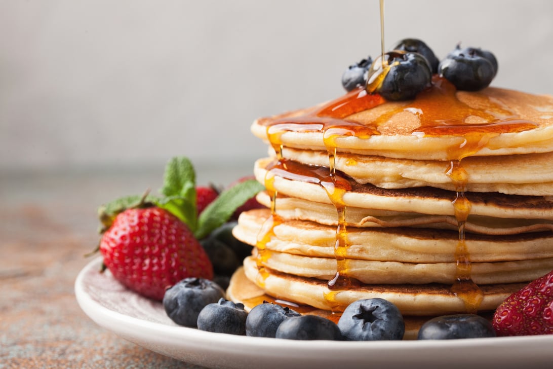 Close-up delicious pancakes, with fresh blueberries, strawberries and maple syrup on a light background. With copy space. Sweet maple syrup flows from a stack of pancake